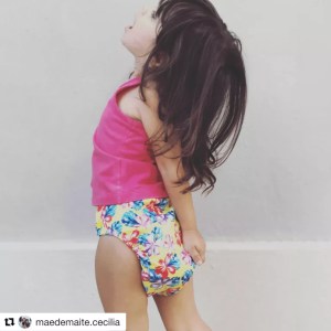 Criança com camiseta rosa e fralda com estampa florida olhando para cima.