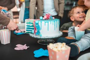 Homem cortando um bolo enquanto uma criança observa sentada à mesa, em um ambiente festivo e alegre.