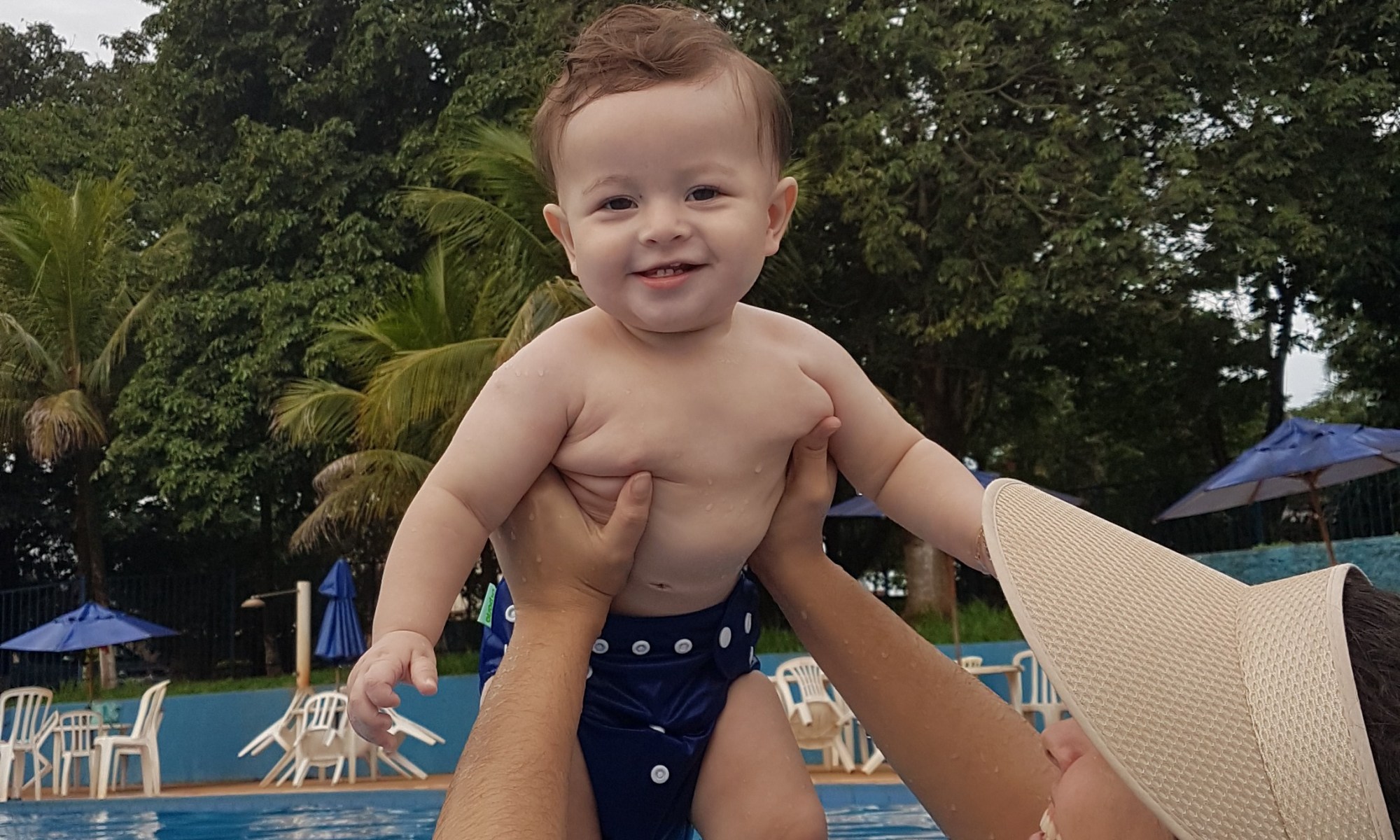 Mulher segurando um bebê na piscina, ambos sorrindo e desfrutando de um momento de alegria e relaxamento.
