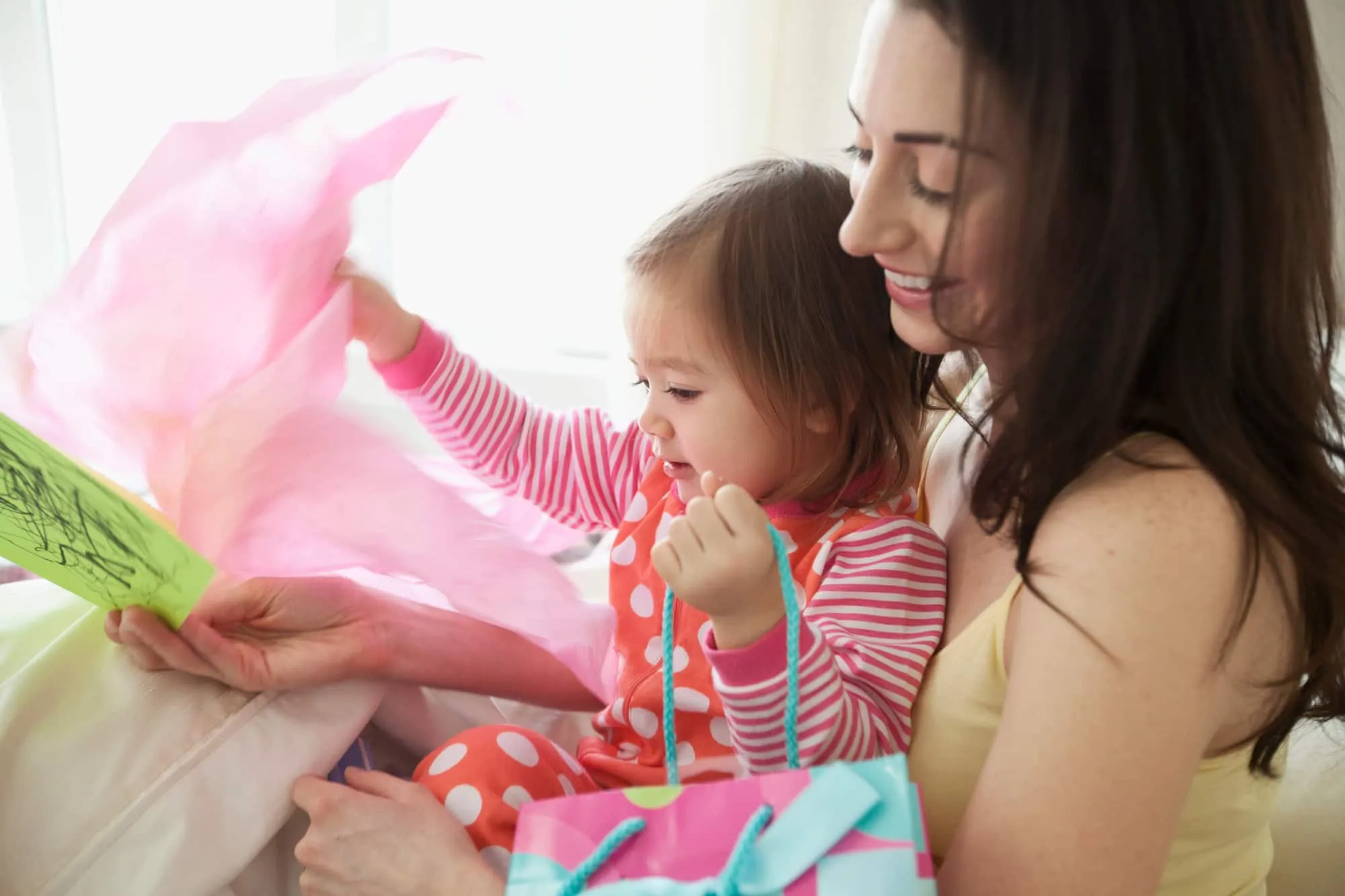 Como surpreender as mães gastando pouco? mulher abrindo um presente com uma criança no colo