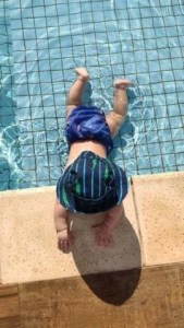 bebê na beira de piscina de chapéu e fralda