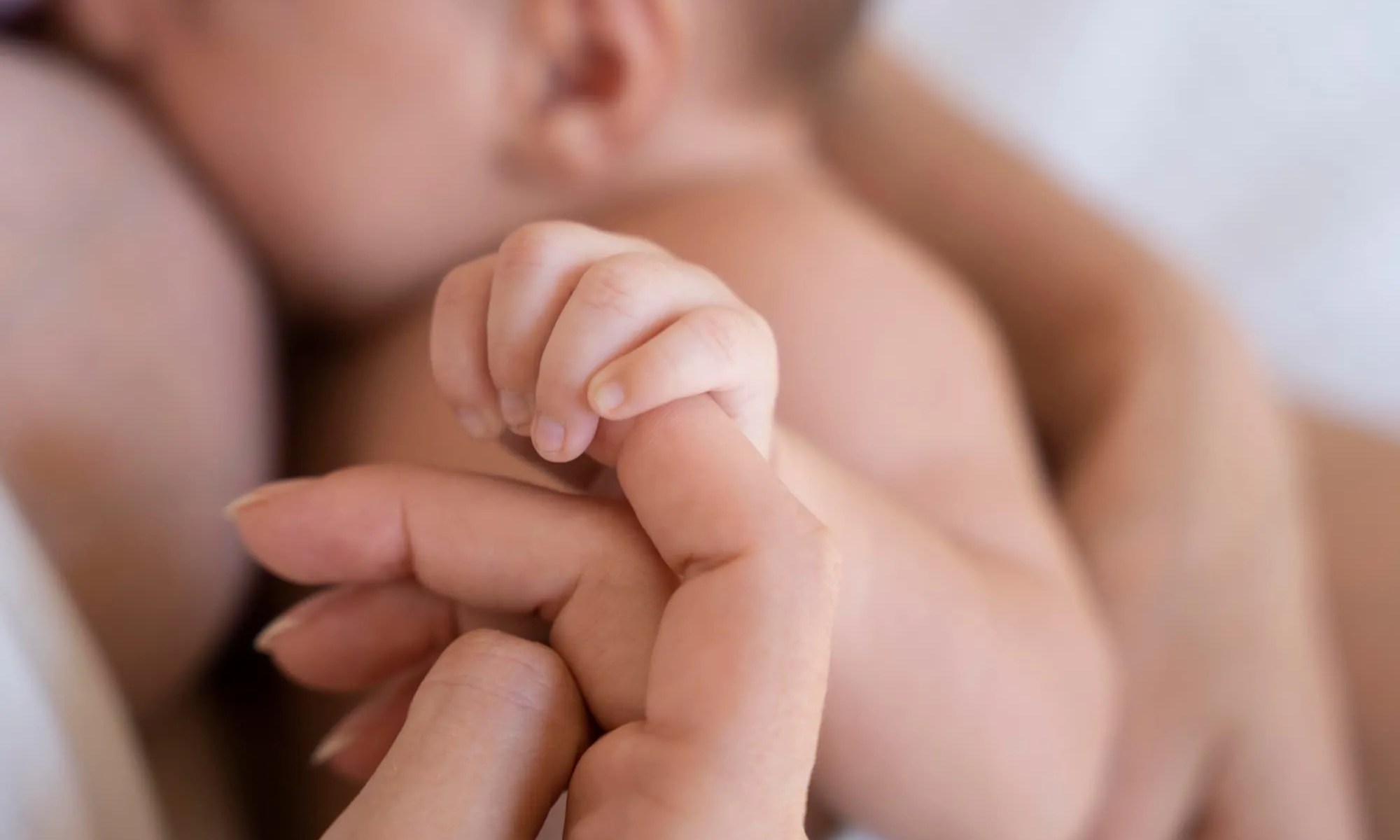 Bebê segurando o dedo da mãe no momento da amamentação.