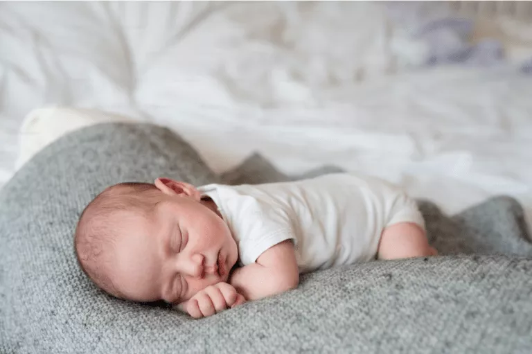 Bebê dormindo de bruços em uma manta cinza.