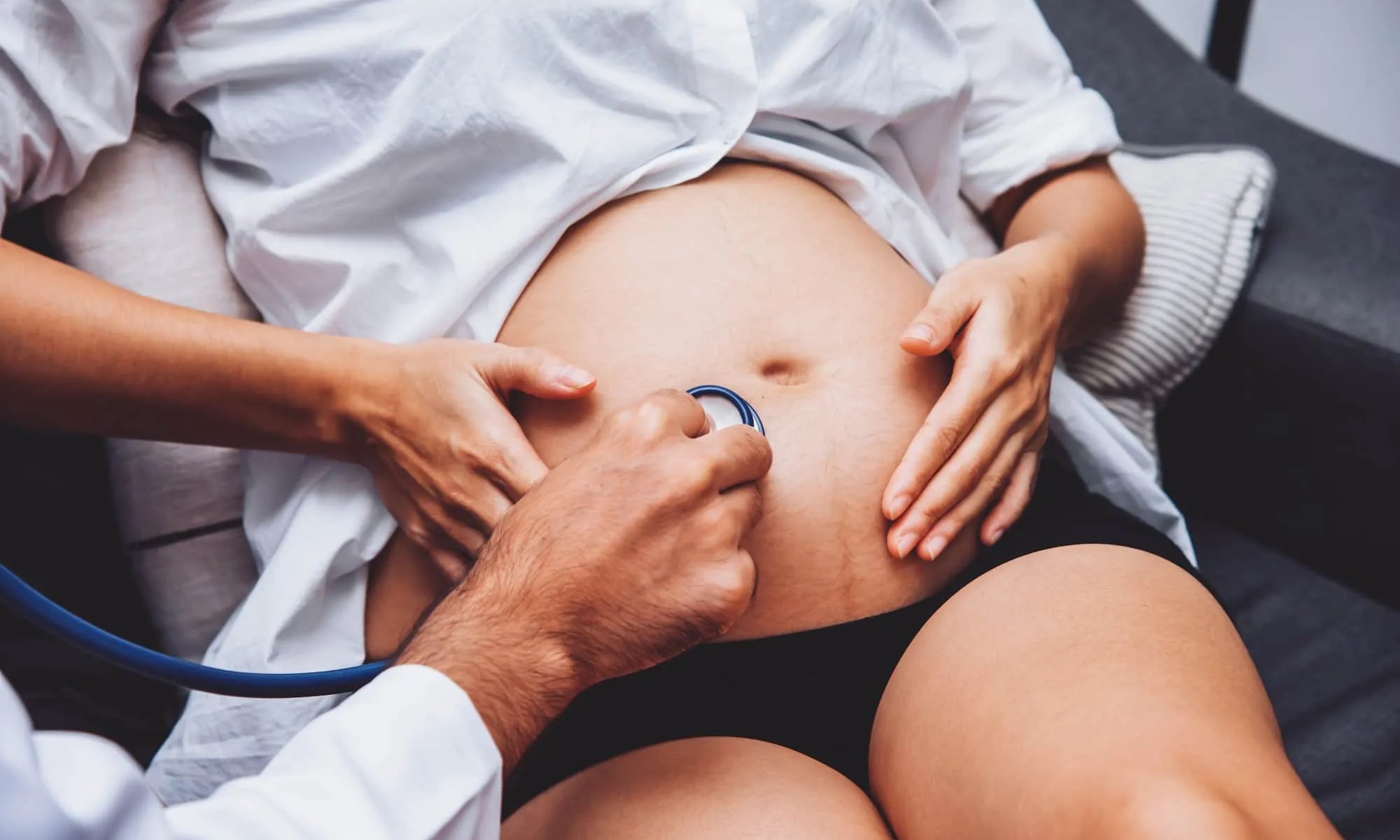 gravida sentada com as mãos na barriga e um médico examinando a barriga