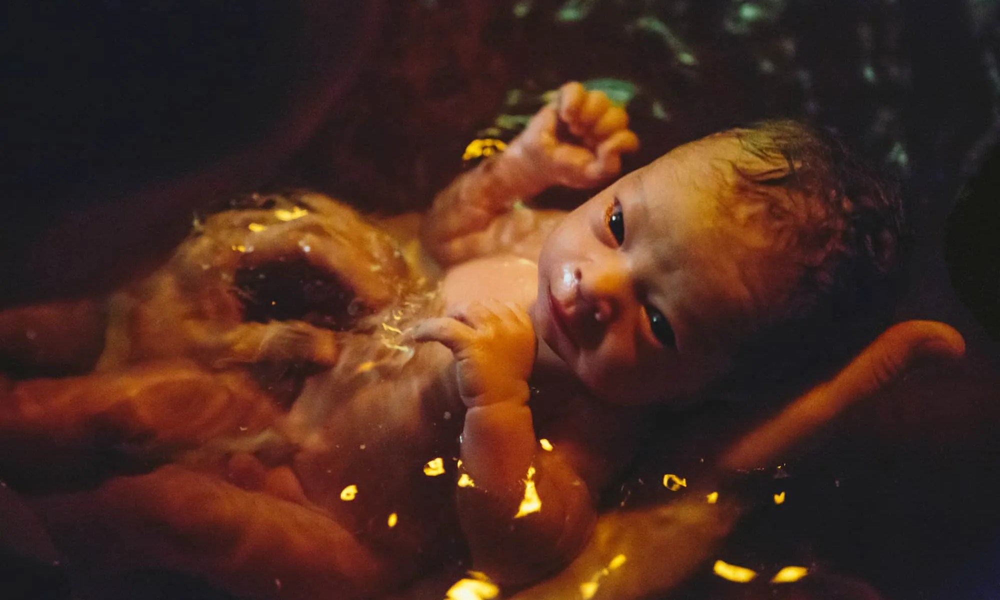 Mãos segurando um bebê na hora do banho.