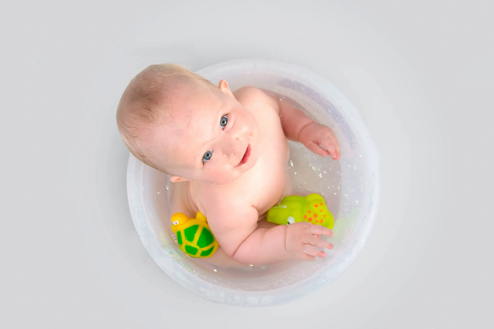 bebê em um balde com água olhando pra cima com brinquedos