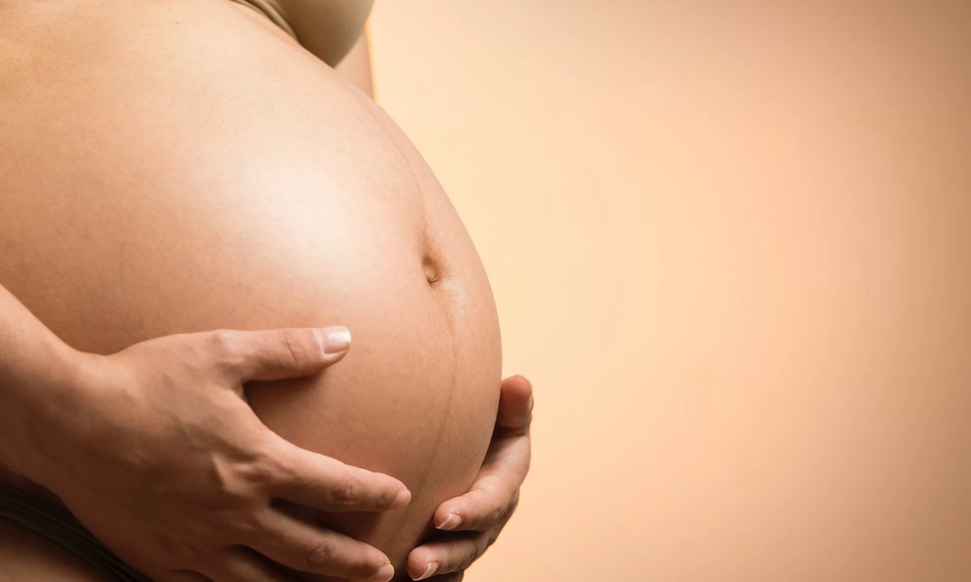 Mulher grávida segurando sua barriga com as duas mãos.