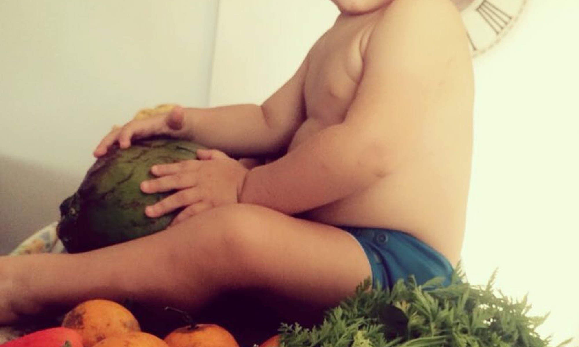 Bebê sentado em uma mesa cercado por uma variedade de vegetais coloridos e frescos.