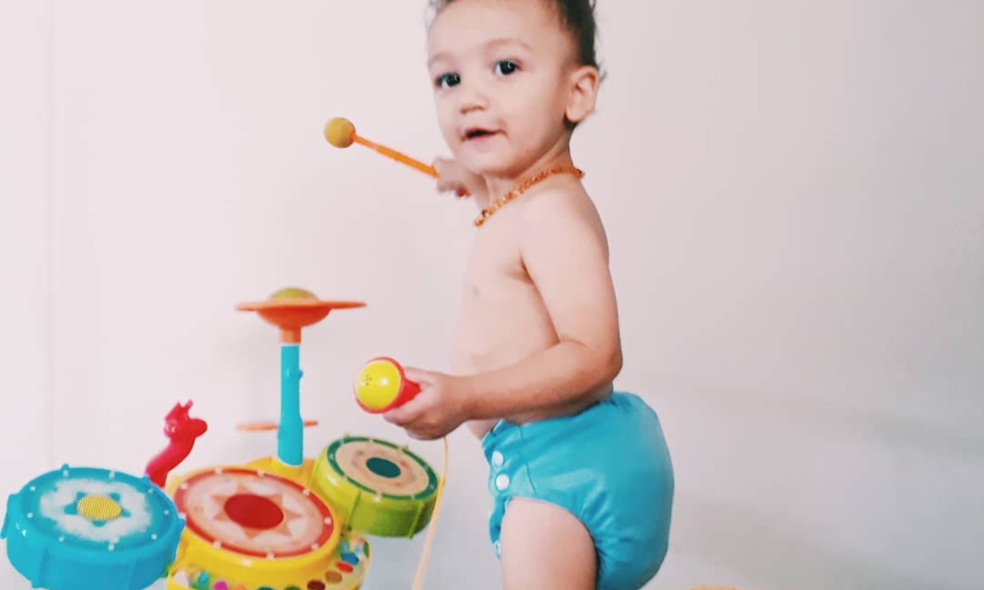 Bebê em fraldas brincando com brinquedos no chão, sorrindo e explorando seu ambiente de forma alegre e curiosa.