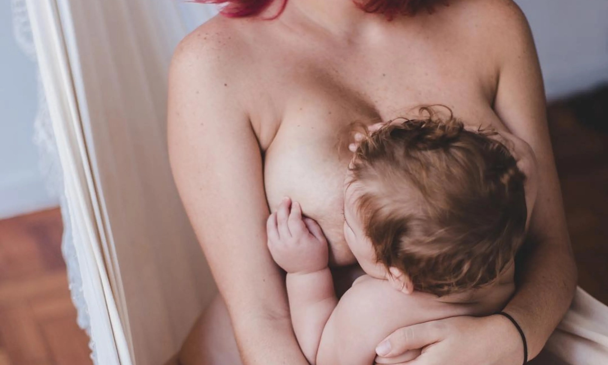 Mulher de cabelo vermelho amamentando seu bebê.