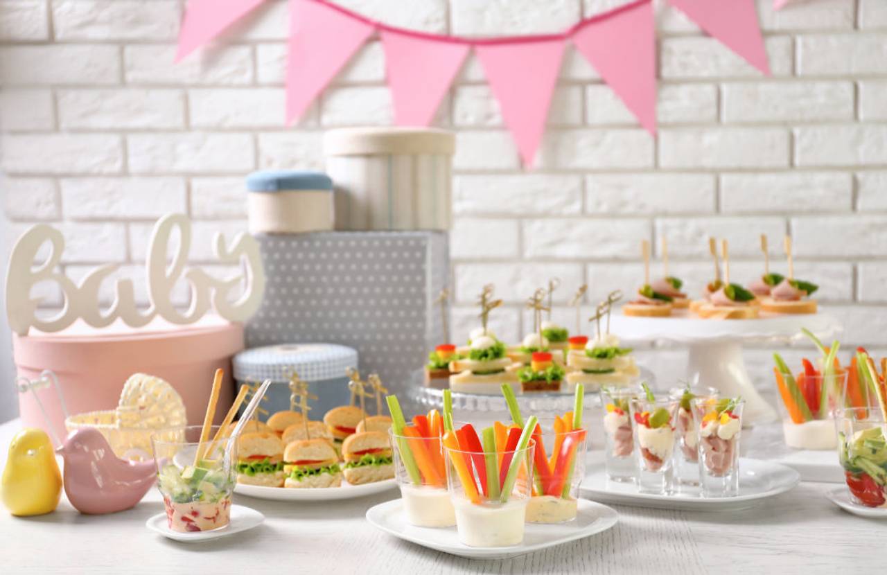 Mesa decorada com alimentos e enfeites para um chá de bebê, criando um ambiente festivo e acolhedor.