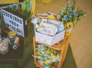 Mesa com uma cesta de itens para bebês e uma placa informativa ao lado, criando um ambiente acolhedor e organizado.