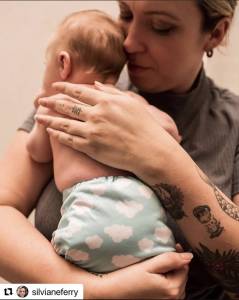 Mulher tatuada segurando um bebê, transmitindo amor e cuidado em um momento íntimo e afetuoso.